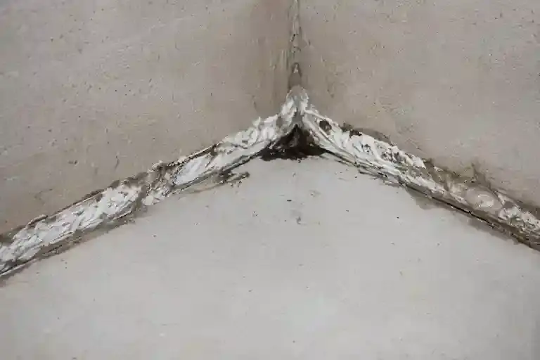 Improperly sealed basement cove joint with deteriorated sealant and moisture intrusion signs.