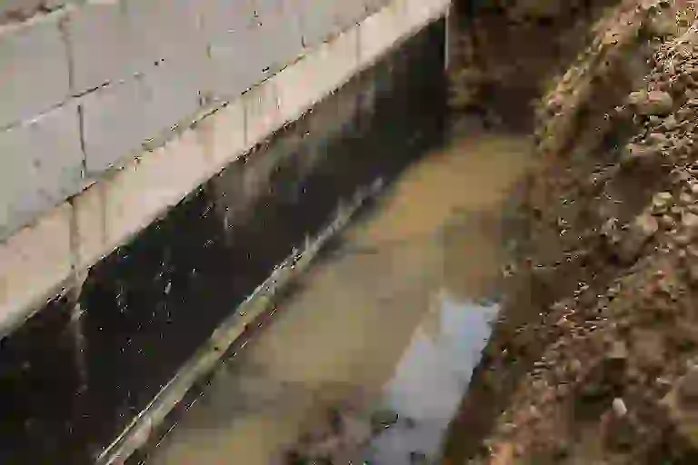 Exterior basement excavation in Ontario showing standing water beside a foundation without proper footing drainage or weeping tile