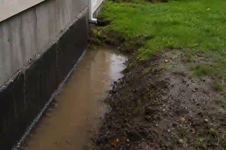 Poor exterior grading near an Ontario foundation causing surface water accumulation beside the basement wall