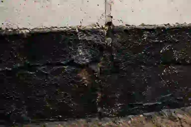 Failed tar-only damp proofing coating deteriorating on an Ontario foundation wall due to groundwater pressure and soil exposure